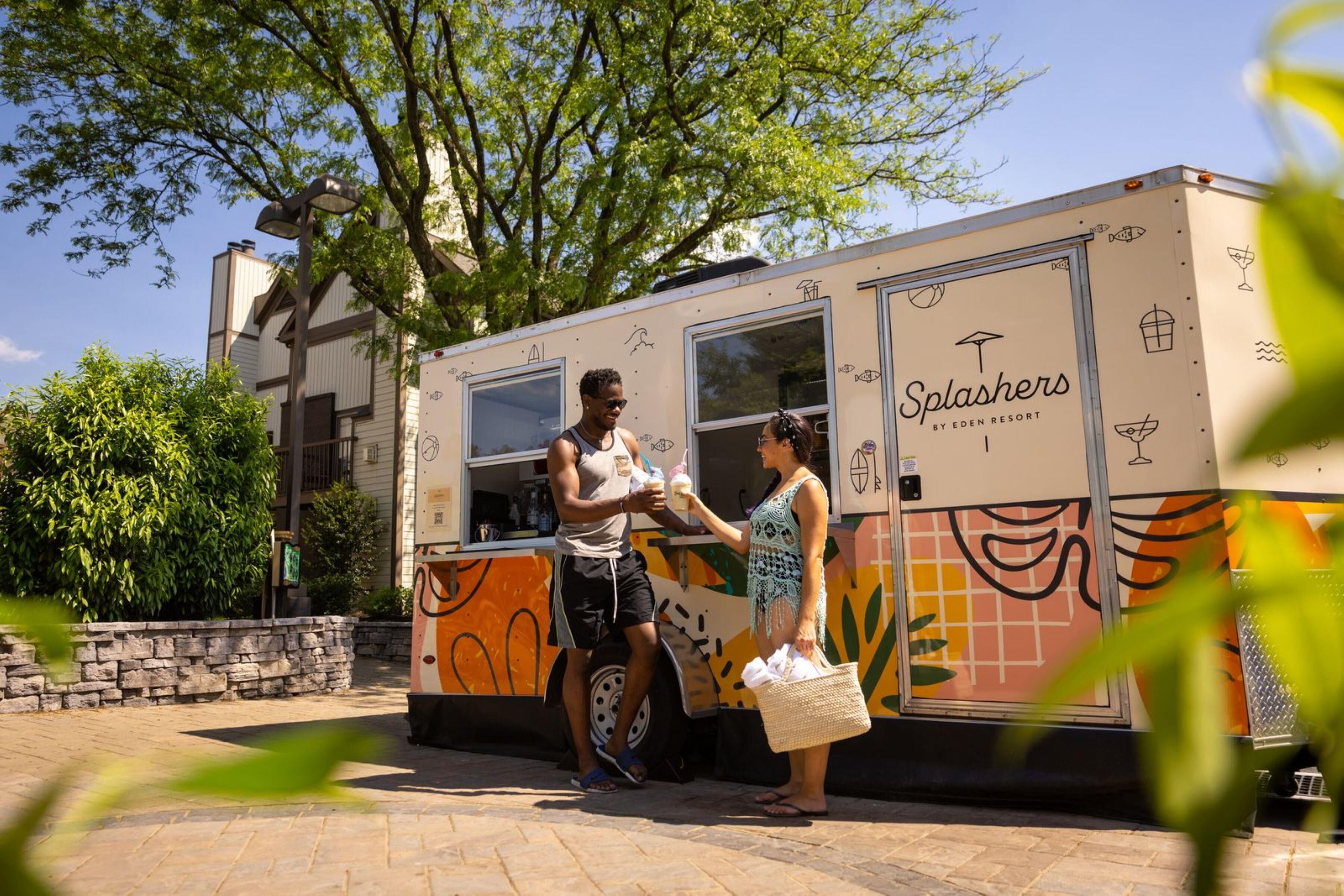 A food truck named 'Splashers' by Eden Resort, parked on a paved area with a stone wall and trees in the background.