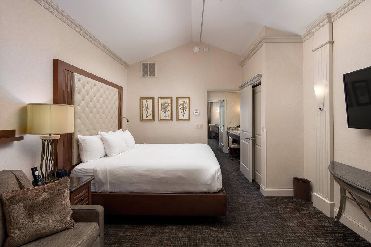 Una habitación de hotel con una cama grande, un escritorio con lámpara, una silla y un televisor en la pared.