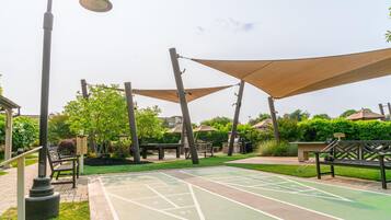 Un patio con una mesa para el juego de hojalata, bancos y estructuras que proporcionan sombra.