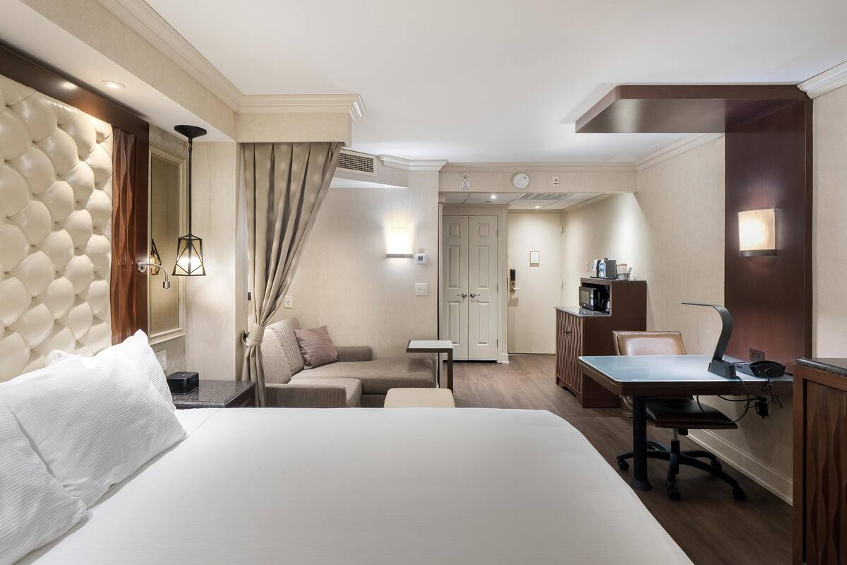 Habitación de hotel con una cama grande, un escritorio con silla, un sofá, una mesita y un microondas.