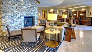 A stone fireplace, seating area with armchairs and a sofa, a small round table, and a reception desk with a vase of flowers. - Eden Resort and Suites, BW Premier Collection (Lancaster)