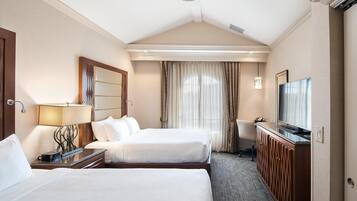 Quarto de hotel com duas camas, uma escrivaninha, uma televisão e um ventilador de teto.