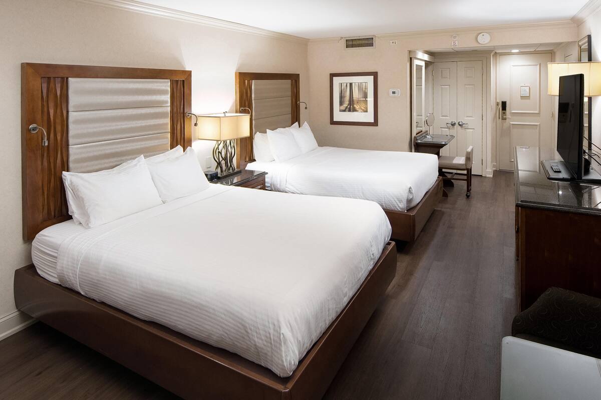 Habitación de hotel con dos camas, un escritorio, una silla, un televisor y la puerta del baño.