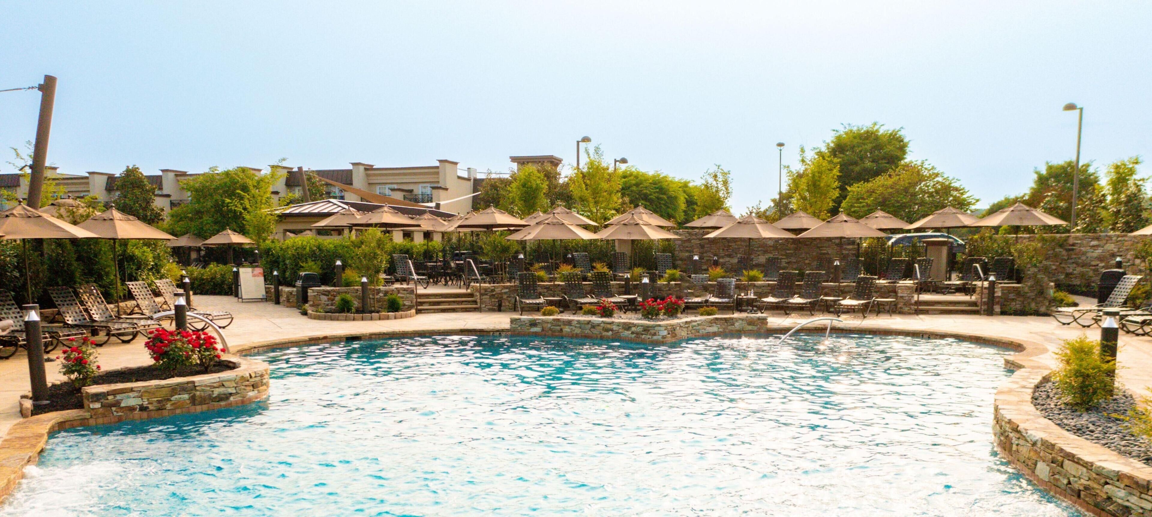 A swimming pool with lounge chairs and umbrellas, surrounded by stone walls and greenery.