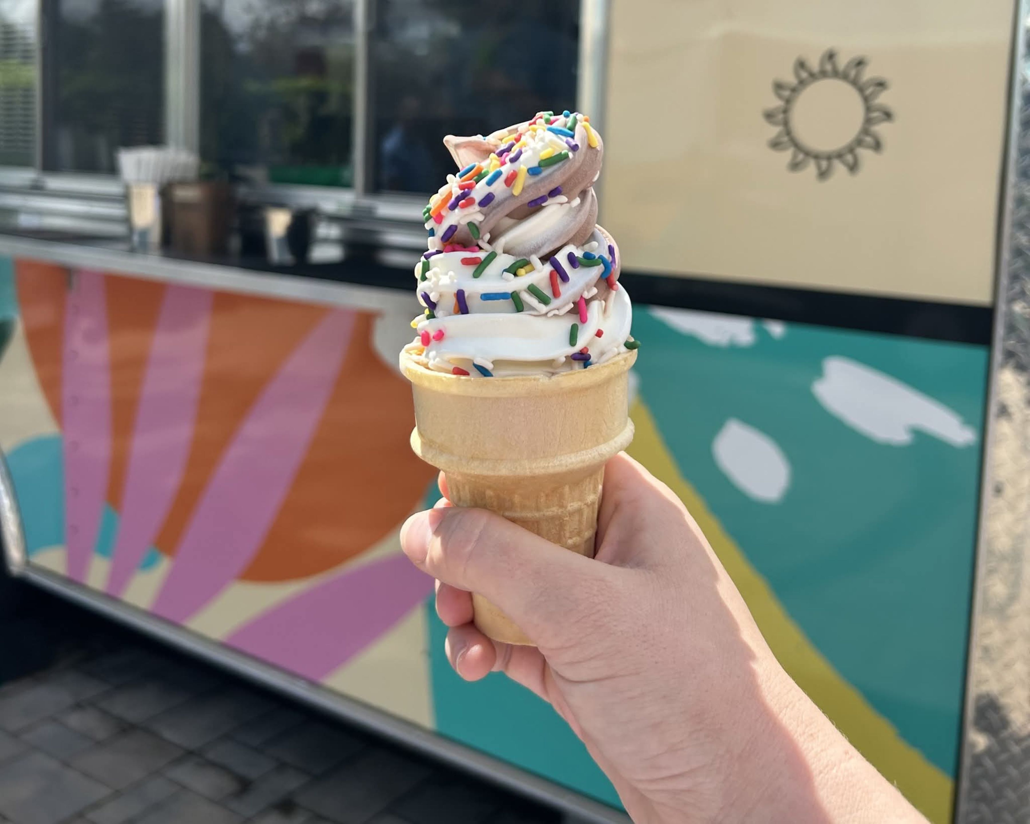 A hand holding an ice cream cone with sprinkles.