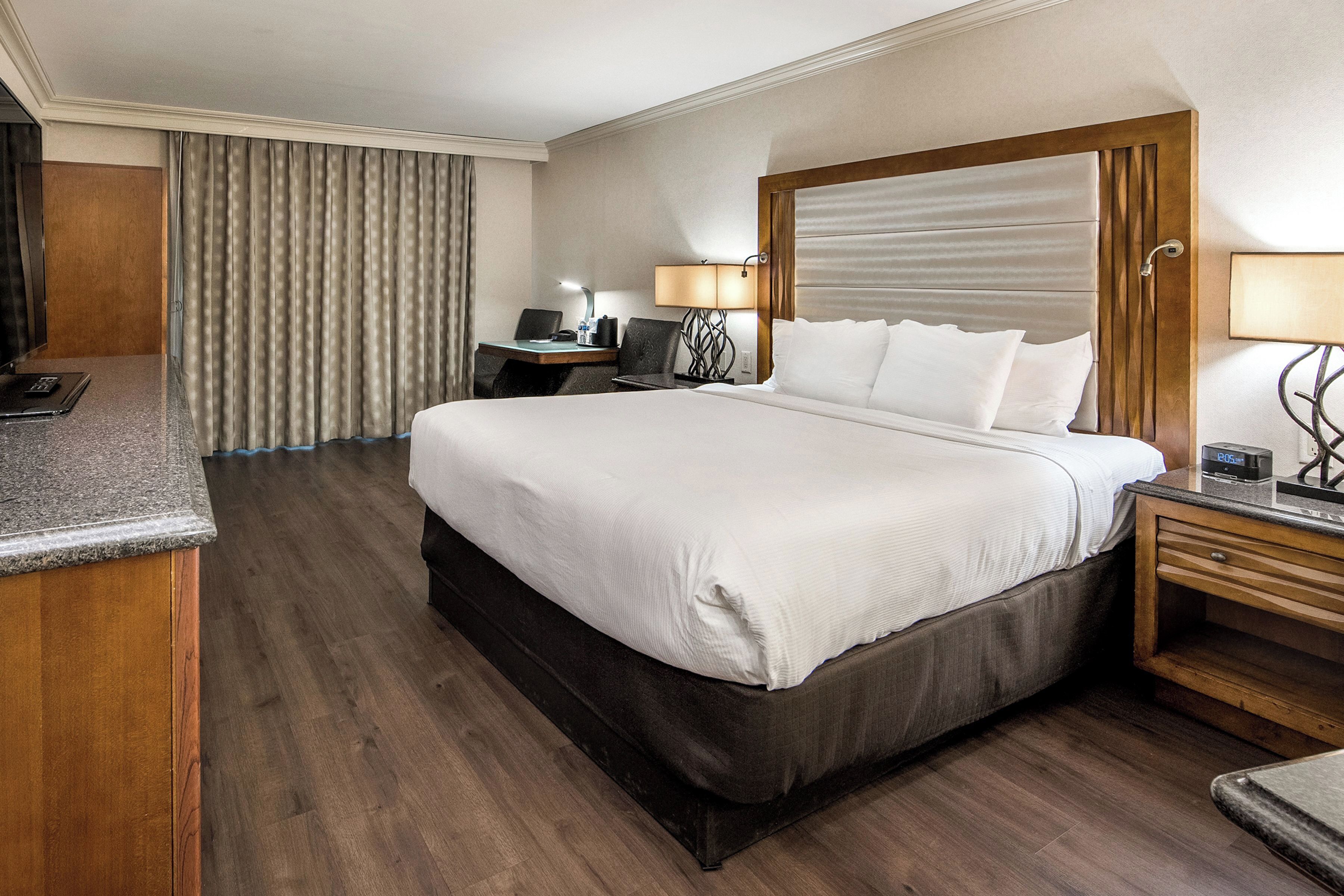 Ein Hotelzimmer mit einem großen Bett, einem Schreibtisch mit Stuhl, einer Lampe und einem Fernseher.