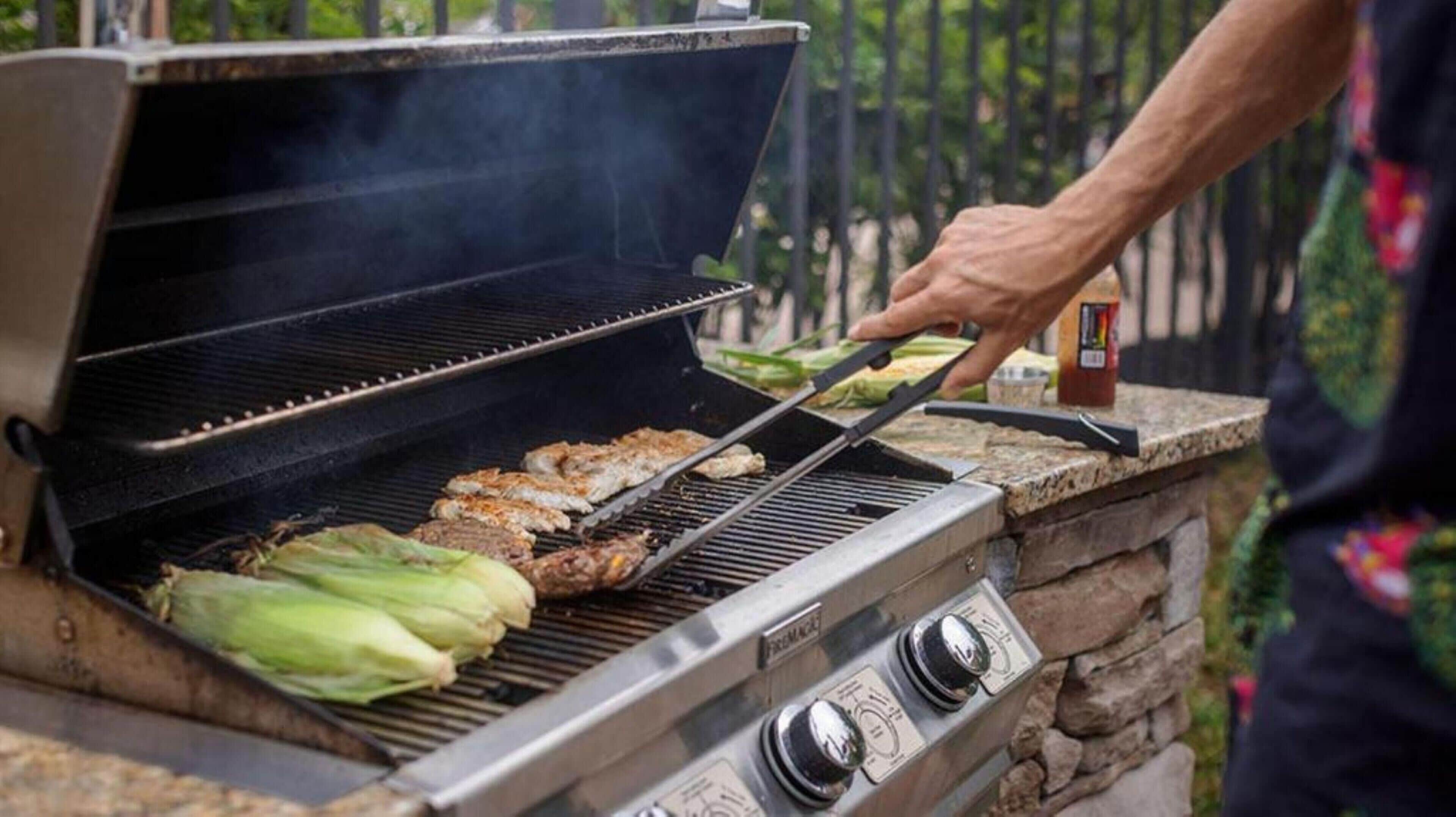 A person grilling food on an outdoor grill with a stone structure and a control panel.