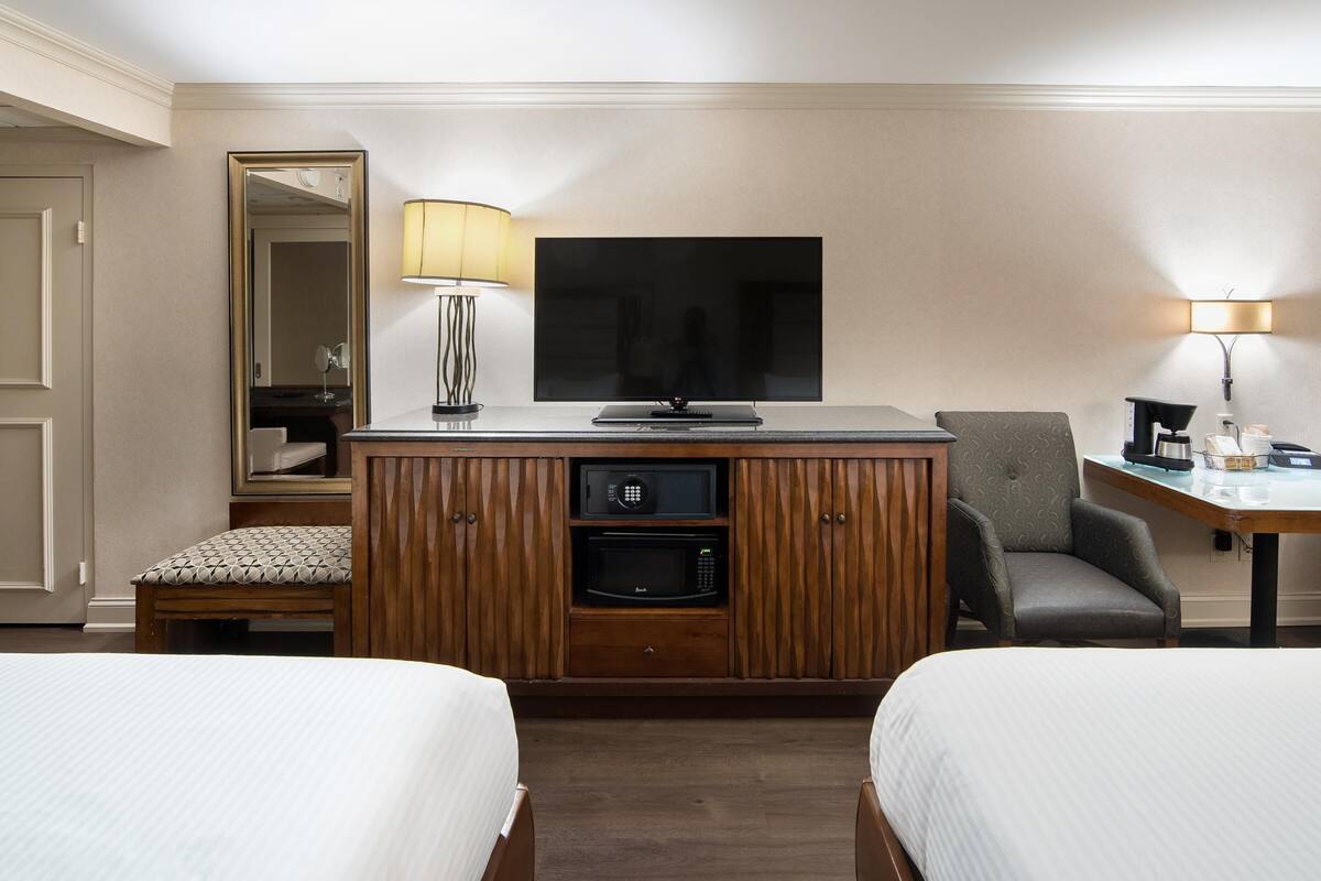 Habitación de hotel con dos camas, un escritorio con lámpara, televisión, microondas y espejo.