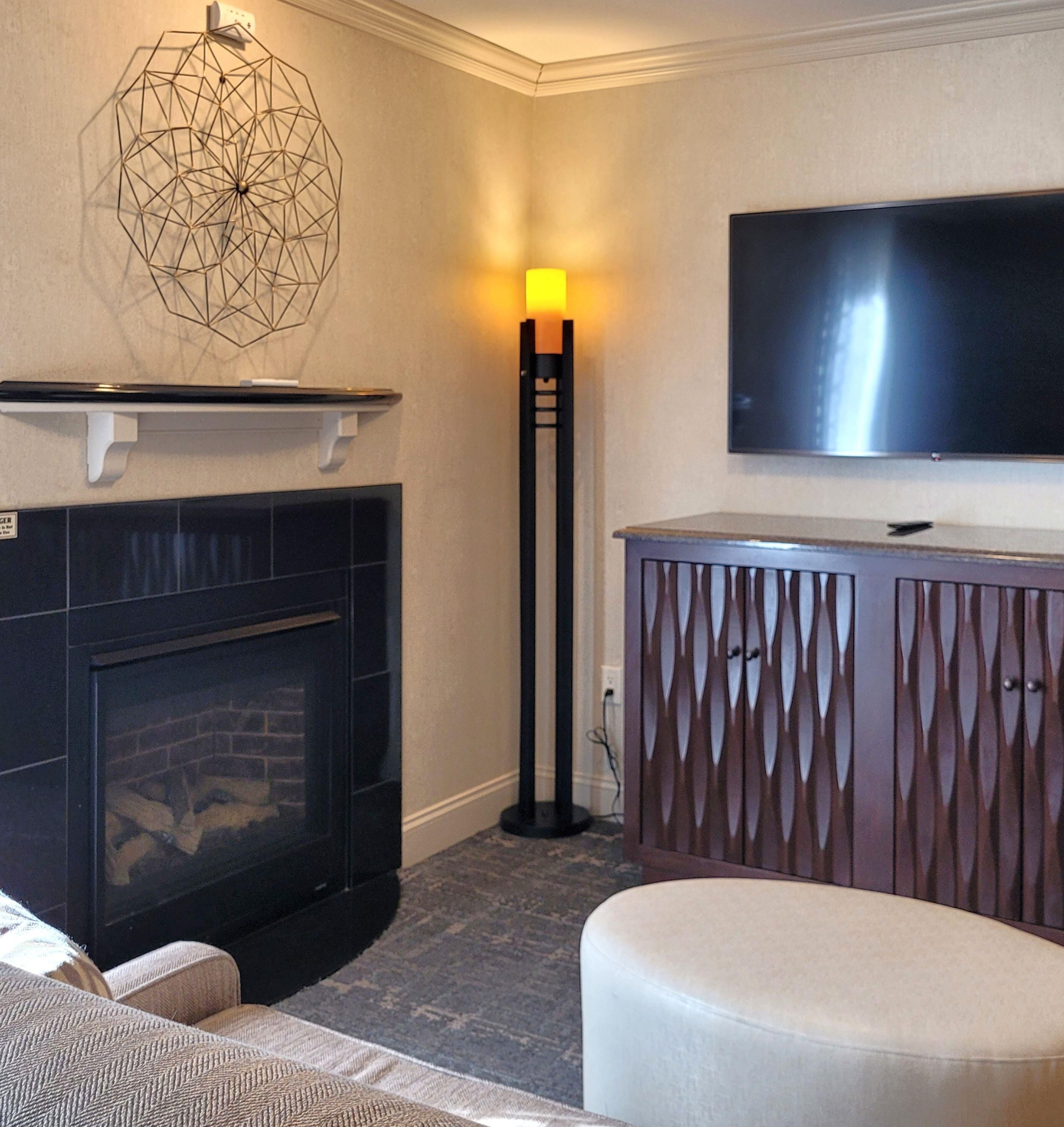 A living room with a fireplace, a TV mounted on the wall, and a patterned cabinet.