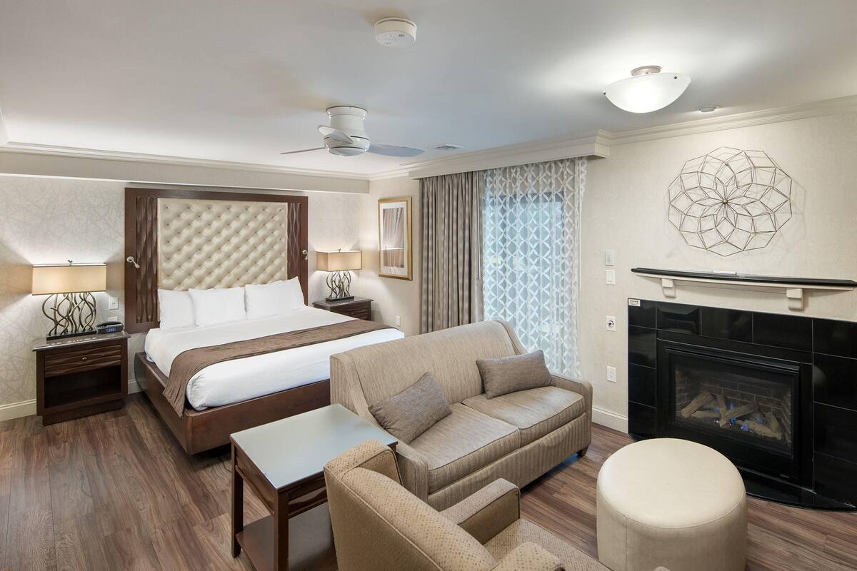 Habitación de hotel con una cama grande, un sofá, una mesita, una chimenea y un ventilador de techo.