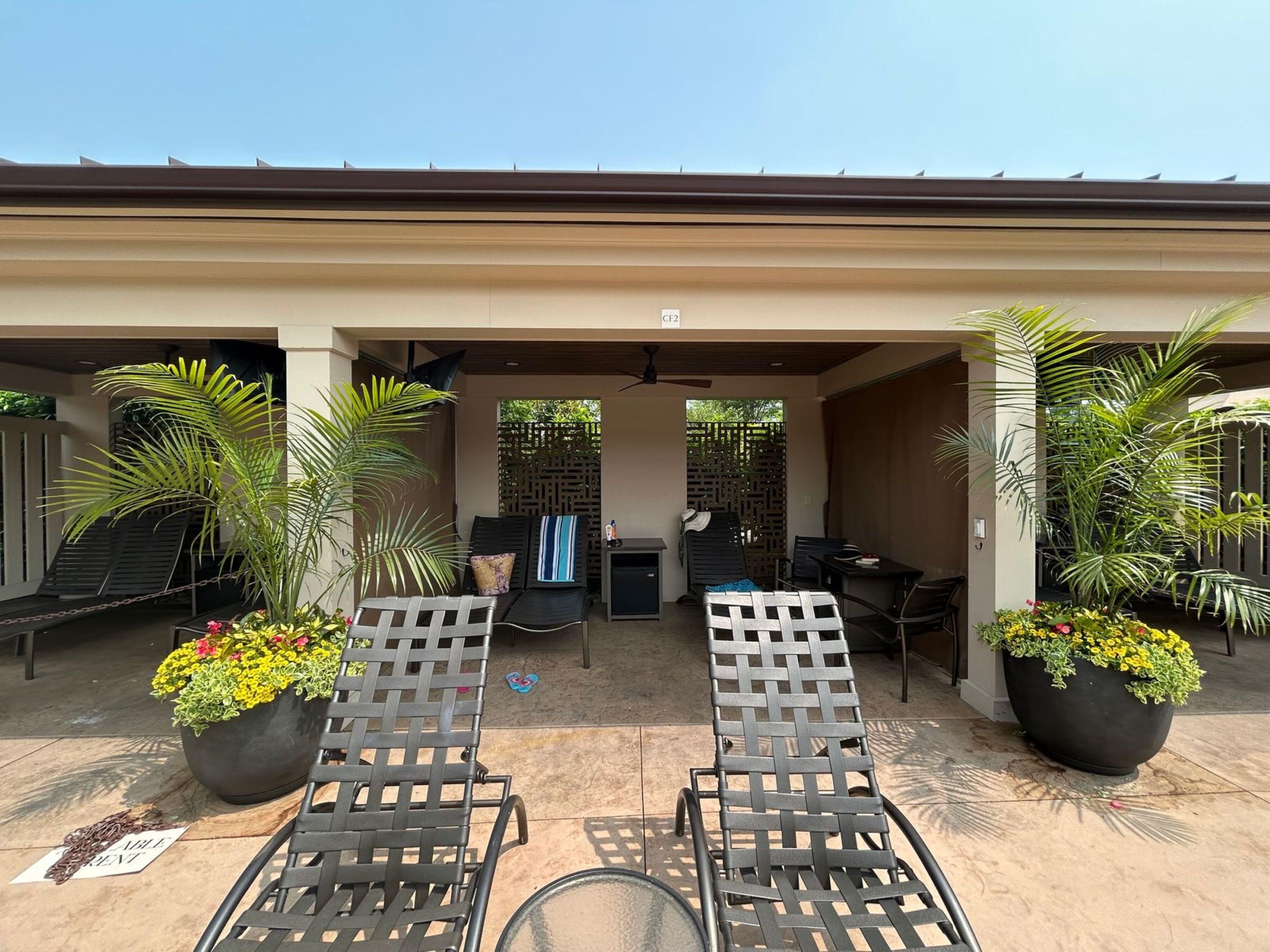 A covered outdoor seating area with lounge chairs, potted plants, and a small table.
