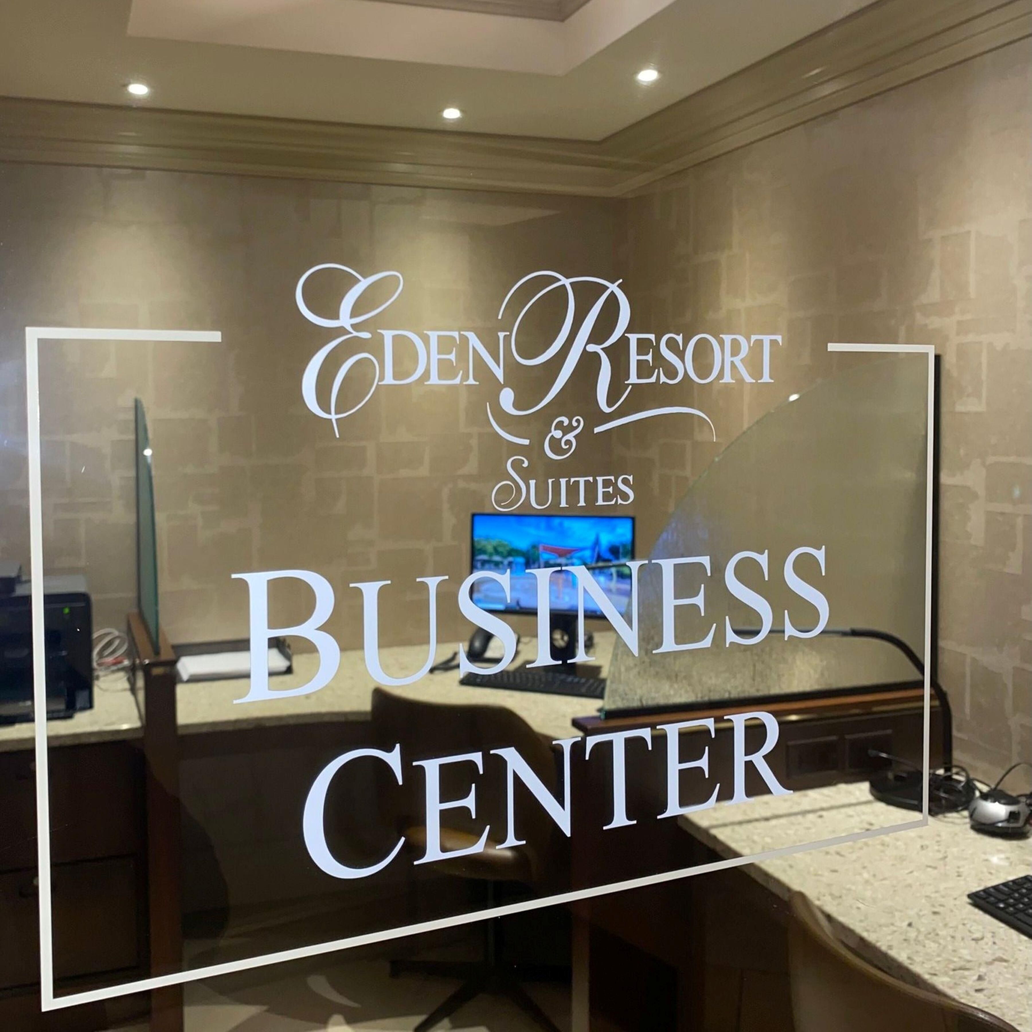 A business center at Eden Resort Suites with a computer, printer, and a television screen.