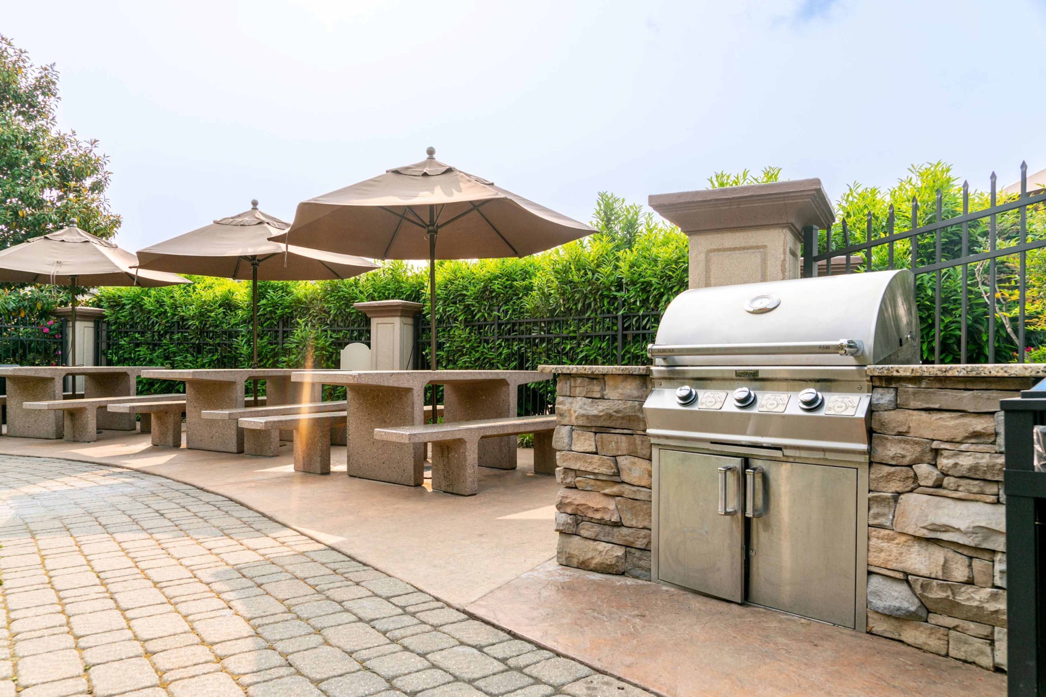 An outdoor patio with stone benches, a grill, and umbrellas.