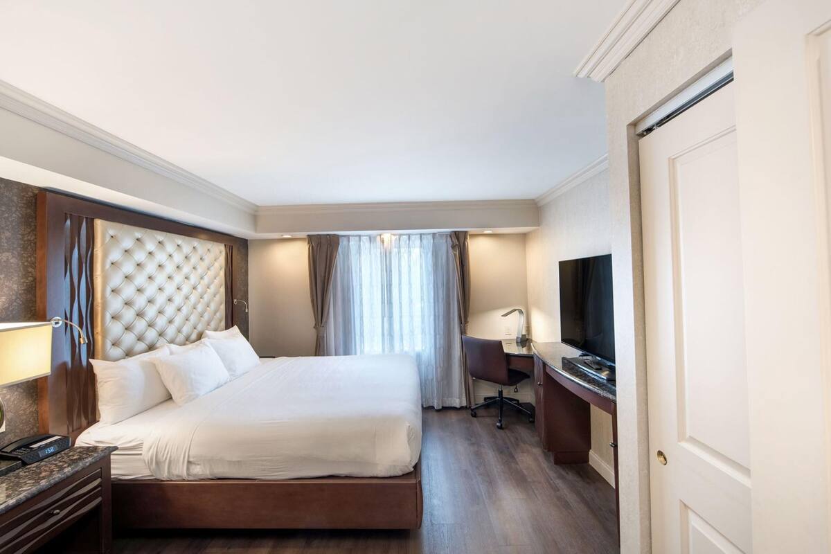 Habitación de hotel con una cama grande, un escritorio con televisor, una silla y una lámpara de escritorio.