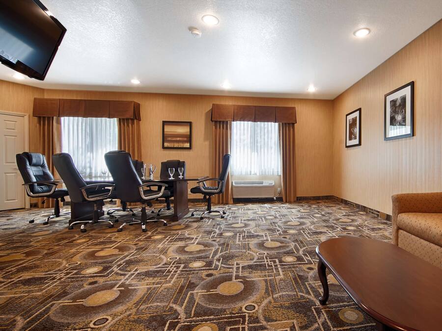 A hotel room with a conference table, four chairs, a sofa, a coffee table, and a TV mounted on the wall.