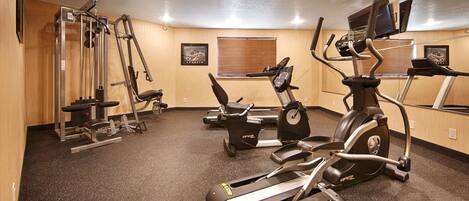 Un gimnasio con máquinas de cardio, pesas y un espejo.