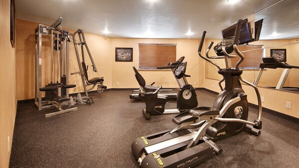 Un gimnasio con máquinas de cardio, pesas y un espejo.