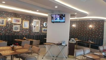 Ein Restaurant mit Sitzecken und Tischen, einem an der Wand befestigten Fernseher und floralem Wandpapier.