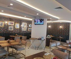 A restaurant with booths and tables, a TV mounted on the wall, and floral wallpaper.