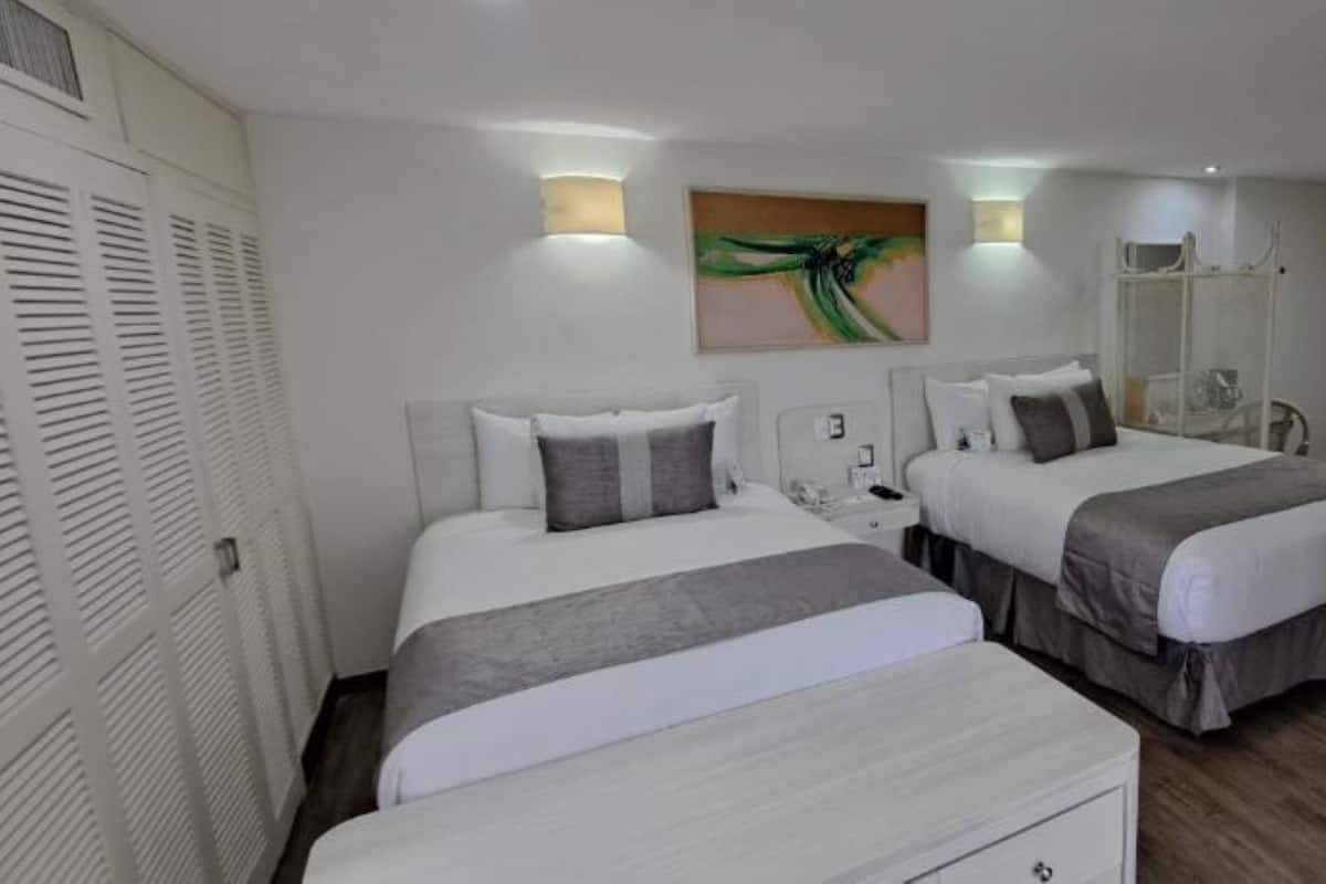 Une chambre d’hôtel avec deux lits, une table de chevet, un miroir et un tableau au mur.