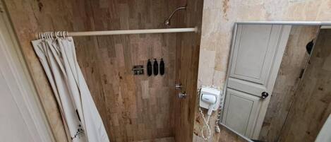 Un espacio de ducha con piso de madera, cortina y puerta.