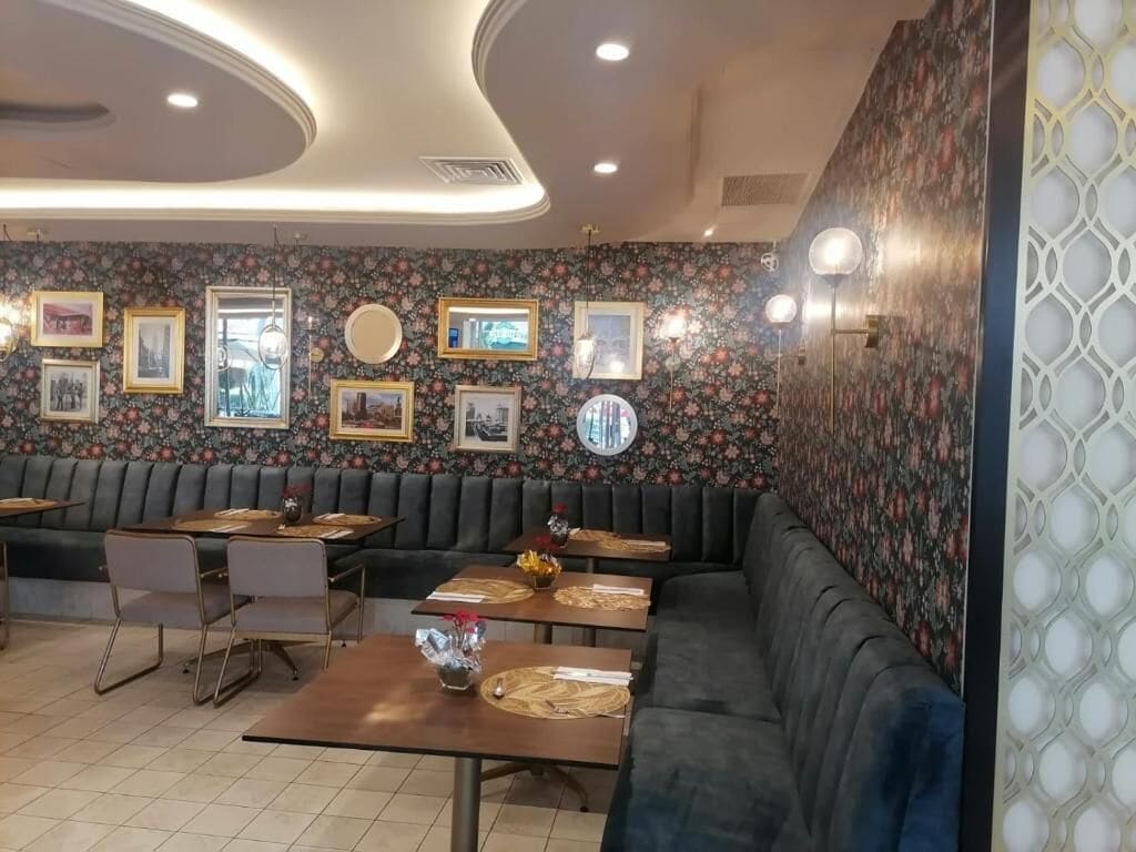 A restaurant interior with a dark green booth seating, wooden tables, and framed pictures on the walls.