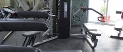 A gym with various exercise equipment including treadmills, weight machines, and a bench.