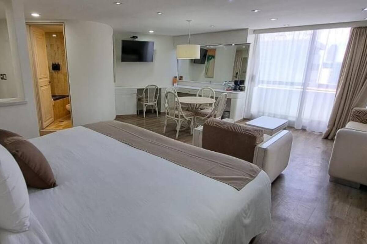 A hotel room with a large bed, a sitting area with a sofa and chairs, a small table, a desk, and a TV.