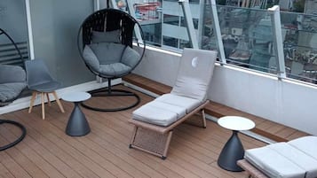 A balcony with wicker furniture, including a lounge chair and a small table.