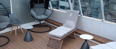 A balcony with wicker furniture, including a lounge chair and a small table.