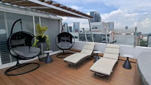 Una terraza en la azotea con dos sillones colgantes, una tumbona y una mesita.
