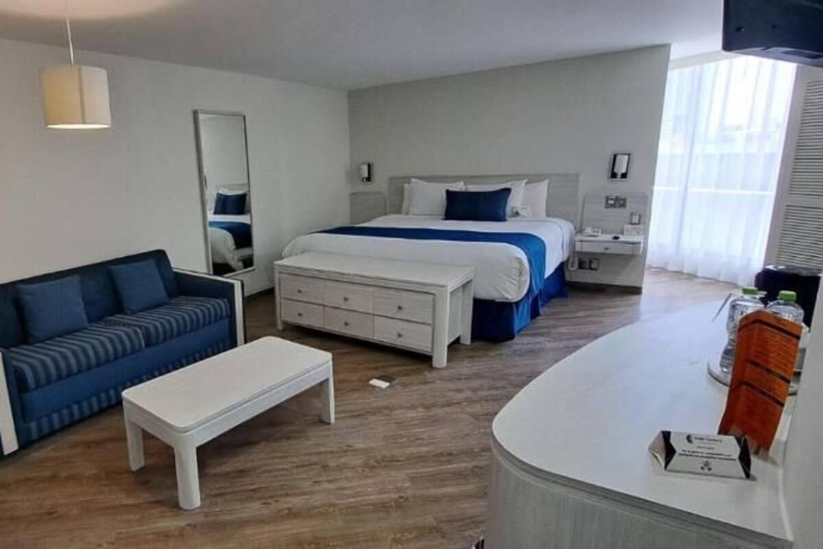 A hotel room with a bed, a sofa, a desk, and a mirror.