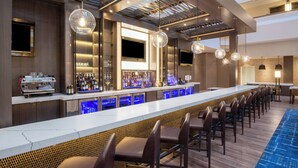 A modern bar area with a long counter, bar stools, and a variety of bottles. - Marriott Madison West (Madison)