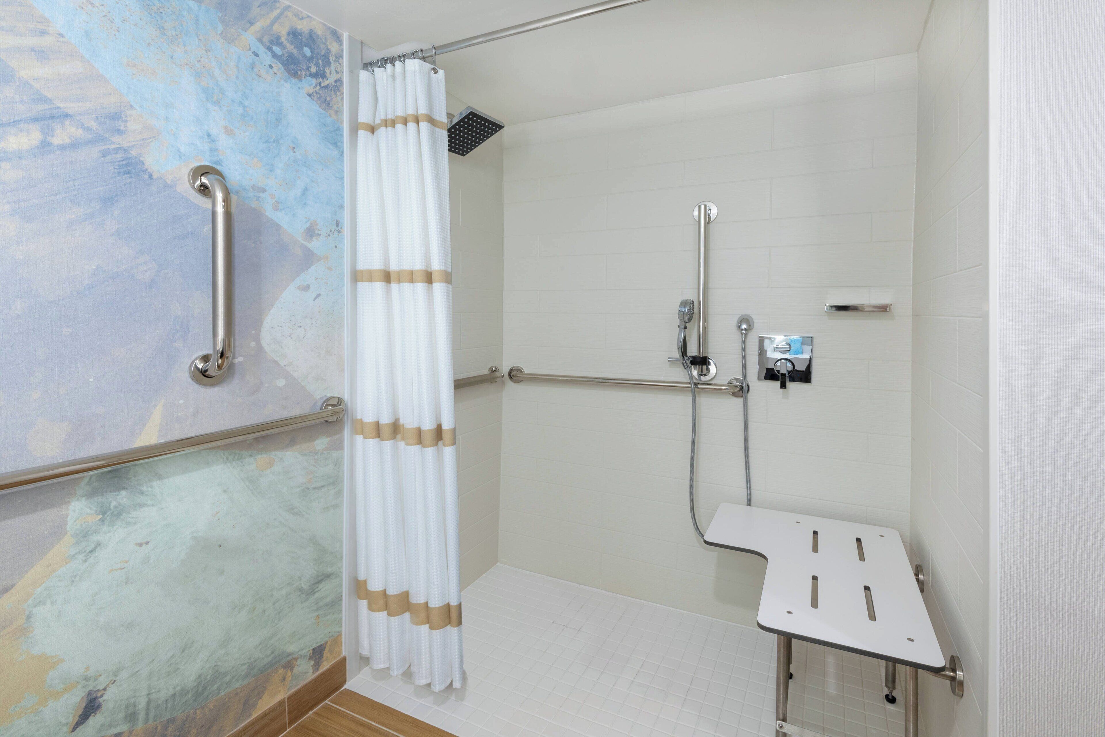 A modern bathroom with a shower, grab bars, and a white tiled floor.