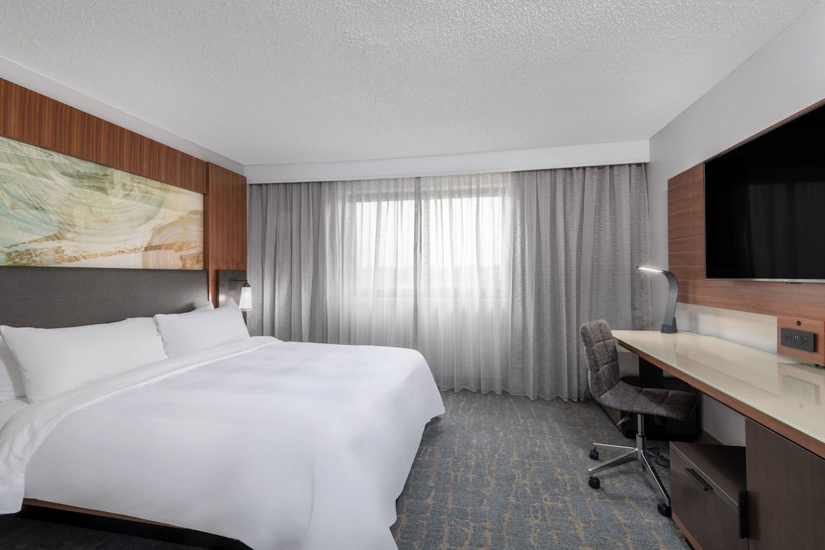A hotel room with a large bed, a desk with a chair, a television, and a window with curtains.