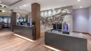 A modern hotel reception area with a wooden reception desk, a digital check-in kiosk, and a decorative wall. - Marriott Madison West (Madison)