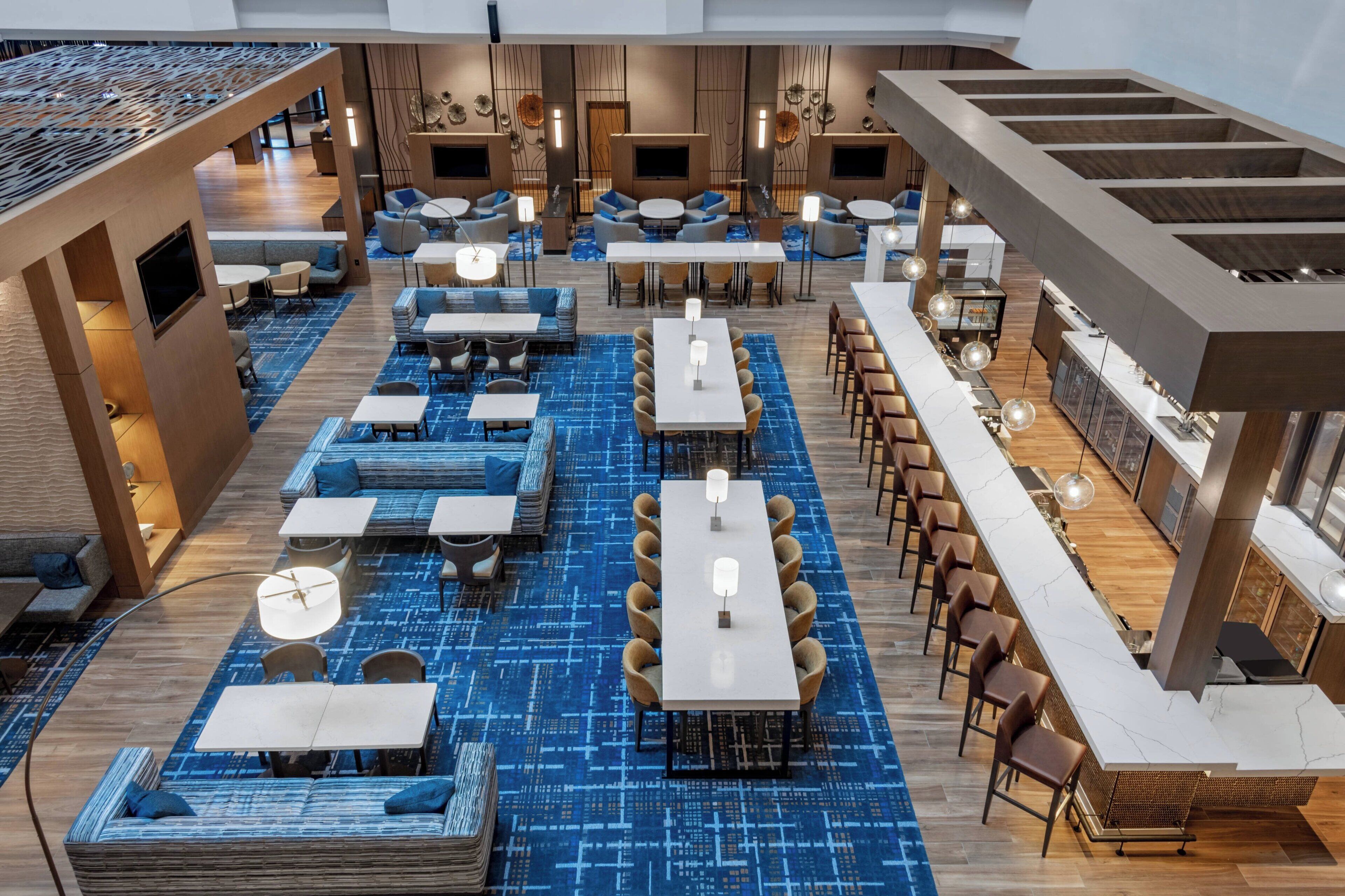 A modern hotel lobby with multiple seating areas, including sofas, tables, and a bar area.