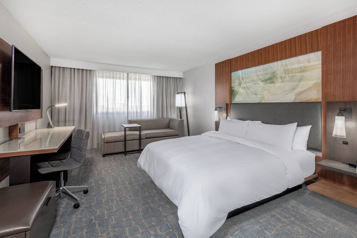 A modern hotel room with a large bed, a desk, a chair, a sofa, and a television.