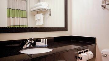 A bathroom with a black countertop sink, a mirror, a towel rack with folded towels, and a toilet paper holder.