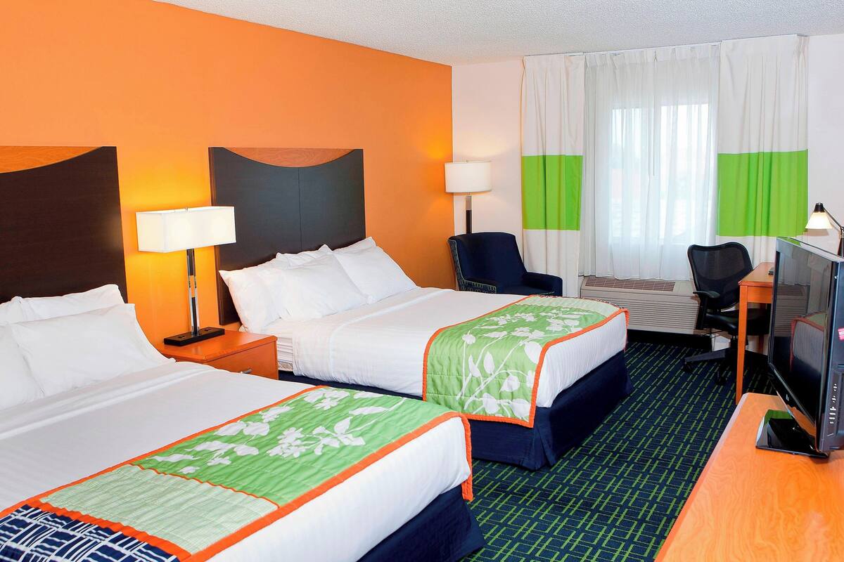 A hotel room with two beds, a desk with a television, and a chair.