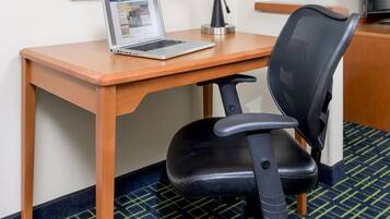 A hotel room with a wooden desk, a laptop, a black office chair, a framed picture of leaves, and a television.