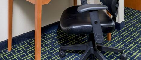 A hotel room with a wooden desk, a laptop, a black office chair, a framed picture of leaves, and a television.