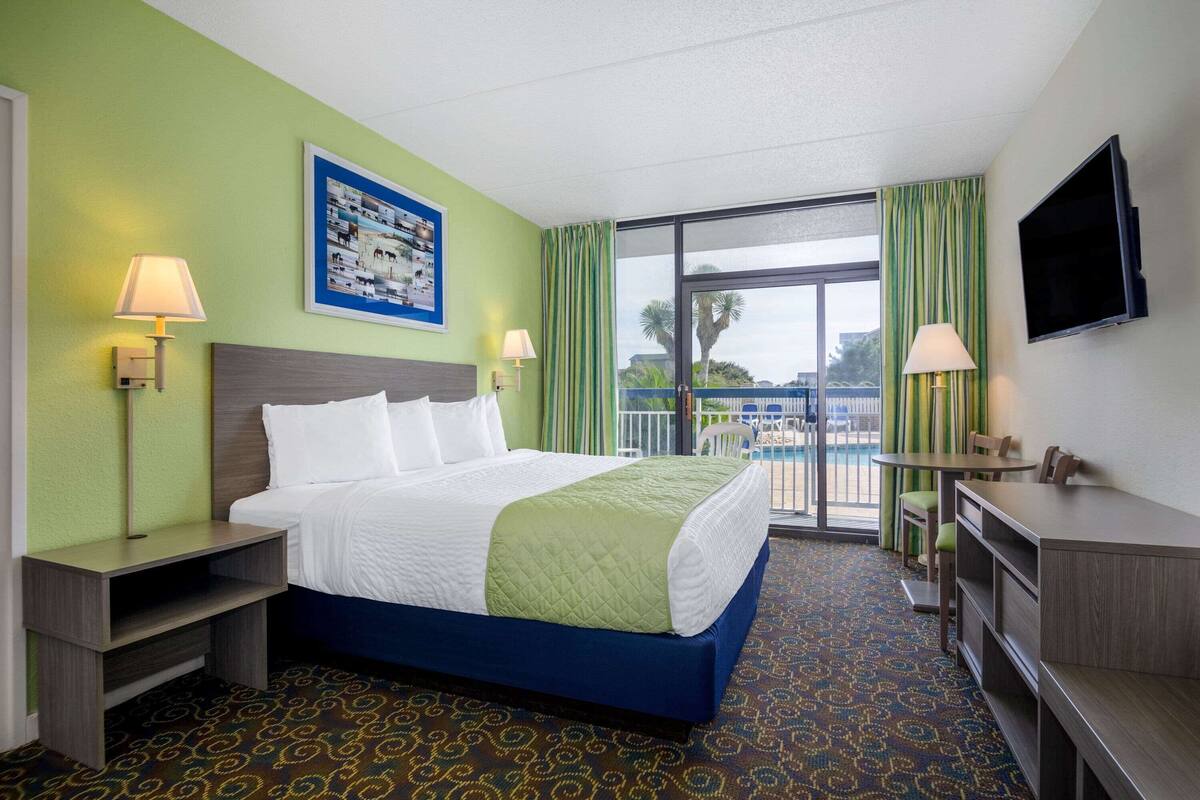 Habitación de hotel con cama, mesitas de noche, escritorio, televisor y vista a una piscina.