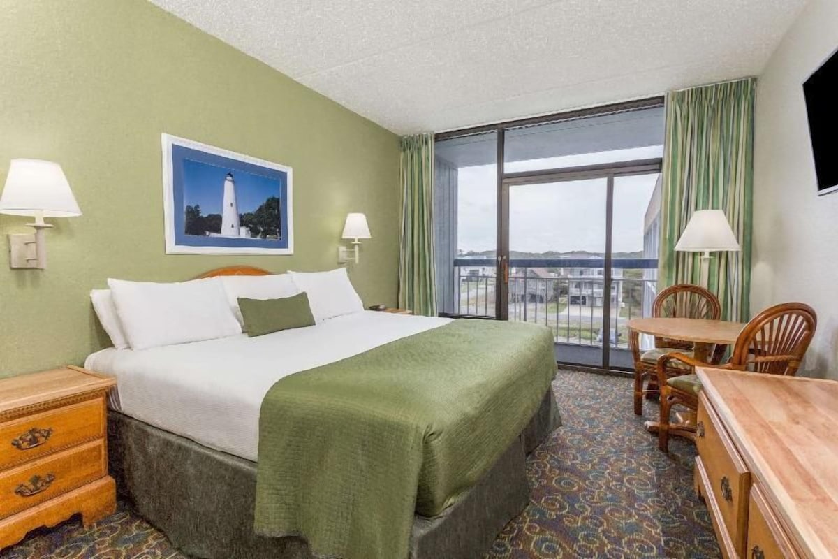 A hotel room with a bed, a desk, a chair, a television, and a window with curtains.