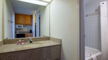 Baño con lavamanos de encimera de granito, espejo, ducha con cortina blanca y microondas sobre el lavamanos.
