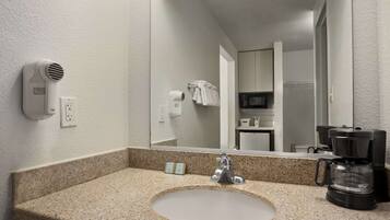 A hotel bathroom with a granite countertop sink, a mirror, a hair dryer, a towel rack, and a coffee maker.