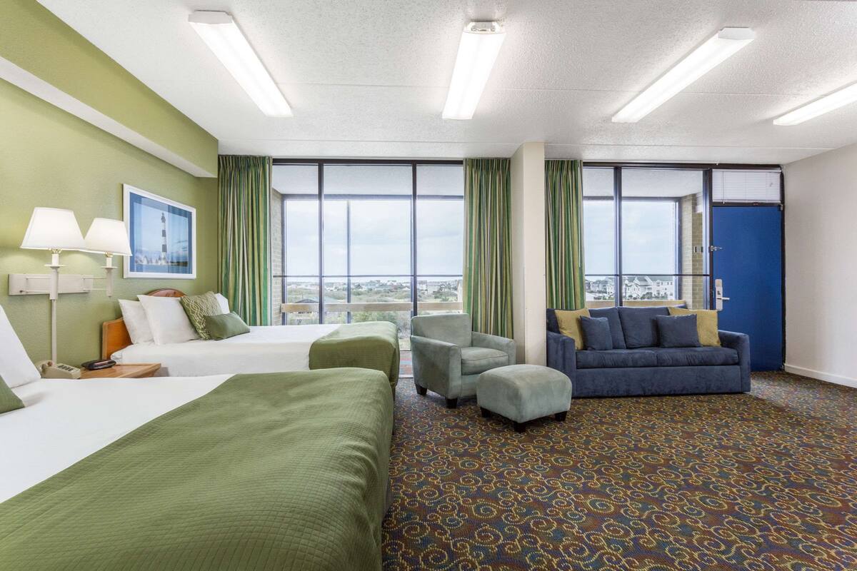 Habitación de hotel con dos camas, un sofá, una silla y vistas a la ciudad.
