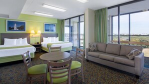 Een hotelkamer met twee bedden, een slaapbank, een eettafel met stoelen, en grote ramen met uitzicht.