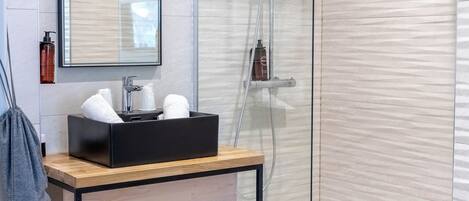 A modern bathroom with a glass shower enclosure, a wooden vanity with a black soap dispenser, and a mirror above the sink.
