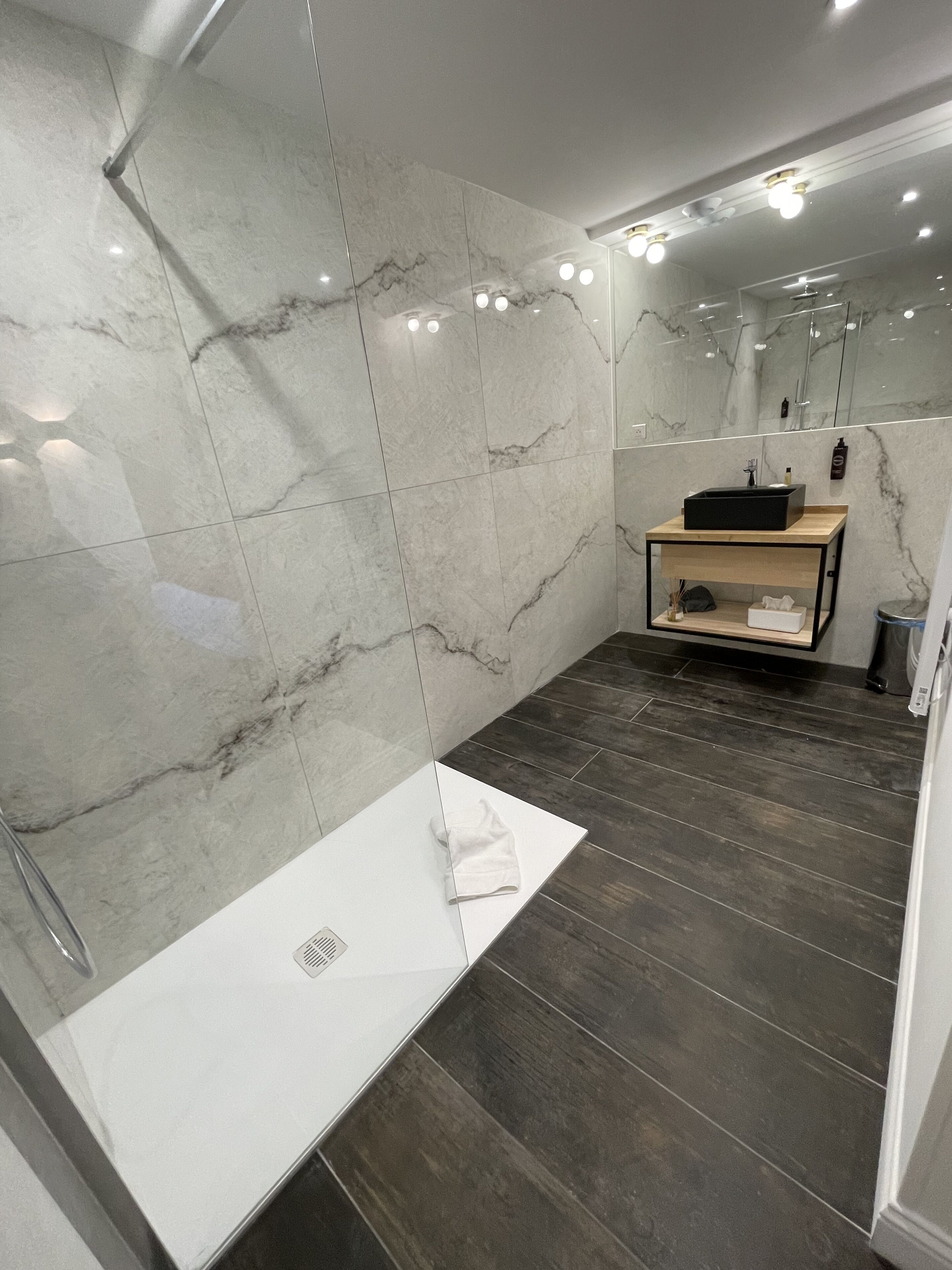 A modern bathroom with a marble wall, a white sink, and a wooden vanity.